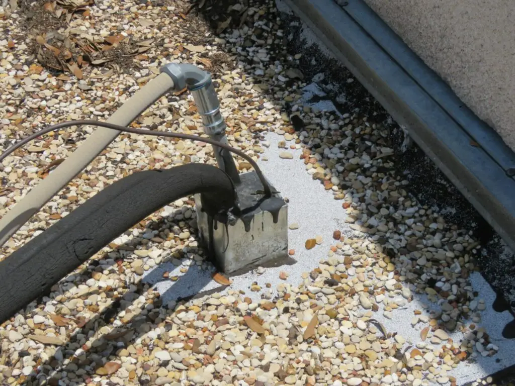 A galvanized steel pitch pan on a built-up roof with multiple small conduits running through it.