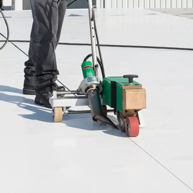 A roofer using a "robot" to heat-weld the seam that joins two sheets of PVC roof membrane.