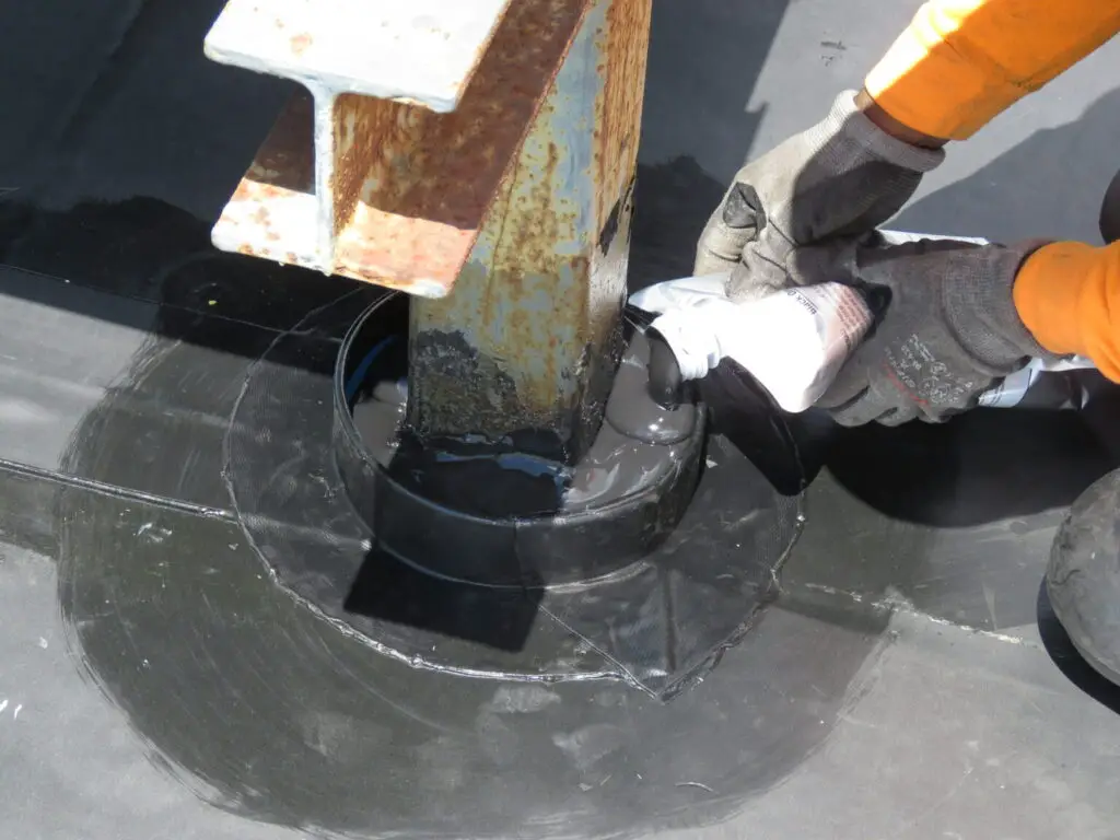 A roofer filling a pitch pan on an EPDM roof with pourable polymeric sealer.