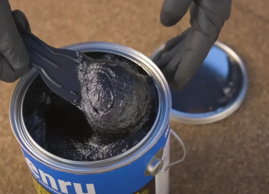 A roofer scooping roof cement out of a can of Henry Wet Patch roof cement.