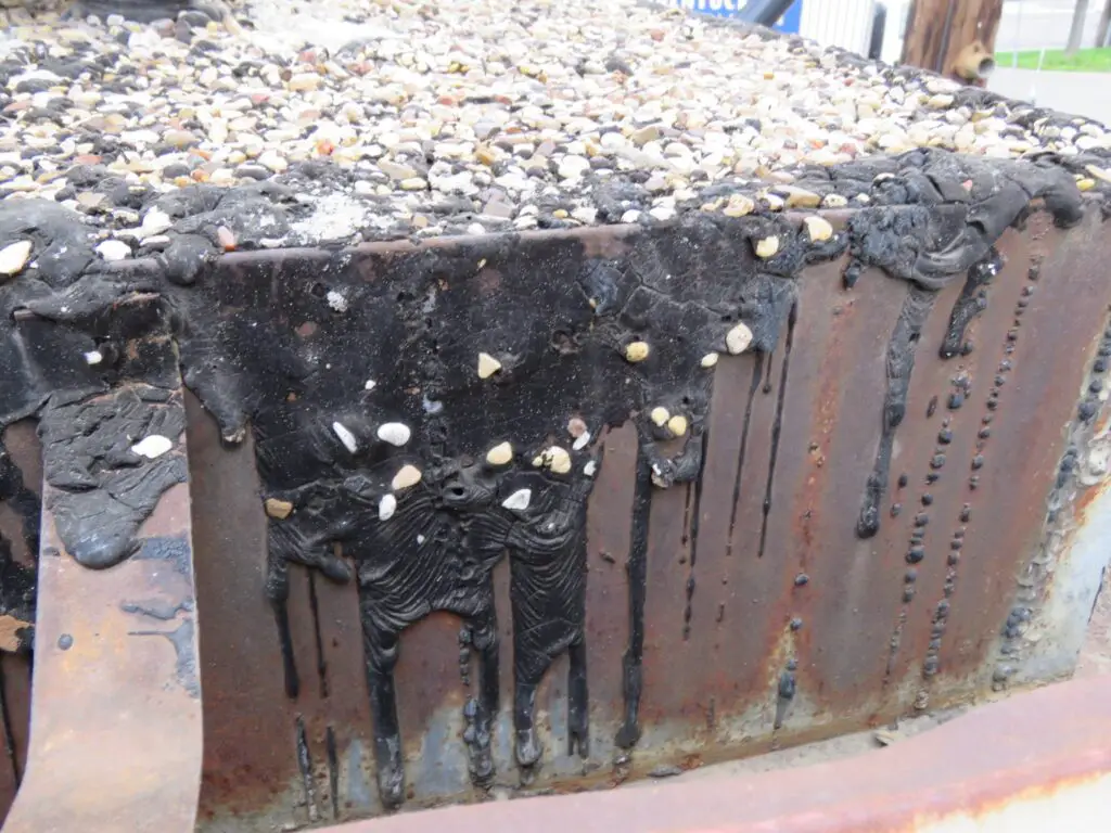 Ripples that have formed in coal tar pitch roofing material on a vertical metal fascia surface.