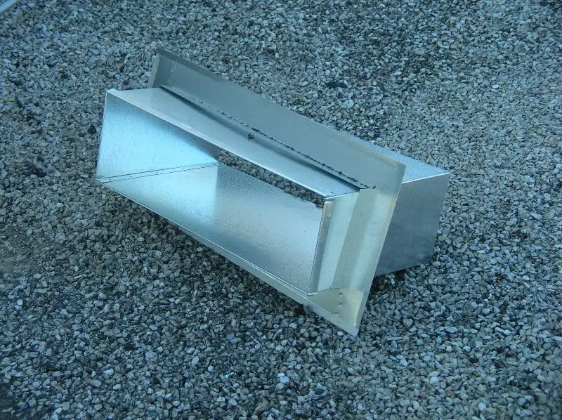 A sheet metal thru-wall scupper box with its exterior faceplate sitting on a roof, ready to be installed.