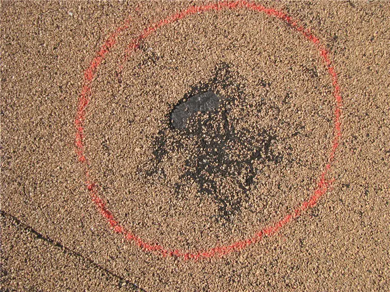 An orange circle around the missing roof granules at the location of a roof blister in a tan-surfaced modified bitumen roof.