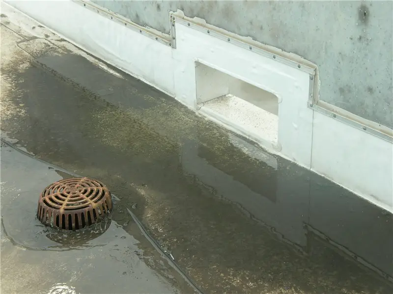 A thru-wall overflow roof scupper in the parapet wall near a roof drain on a low-slope TPO roof.