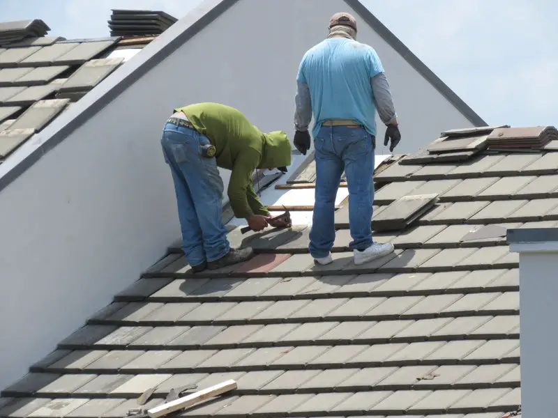 Two roofers repairing a concrete tile roof.