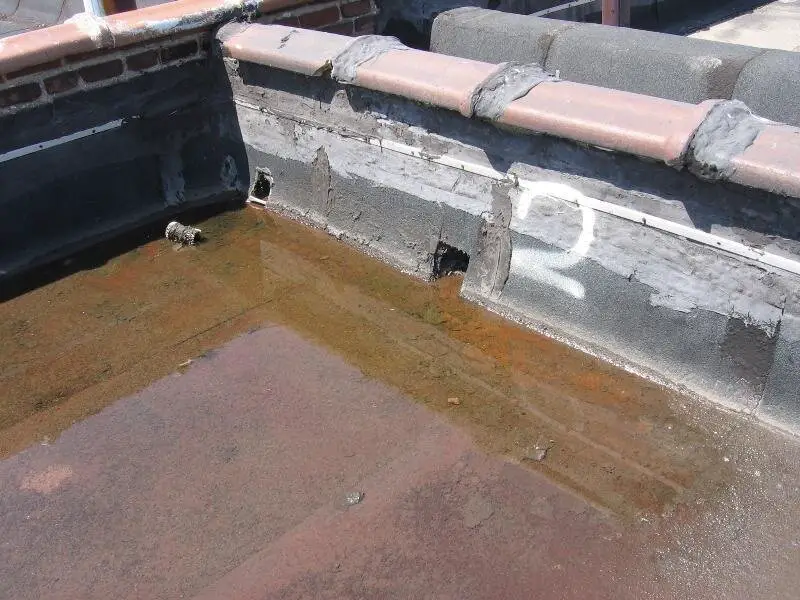 Ponding water on a roof near scuppers through a wall separating two roof sections on the same building.