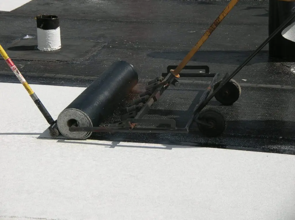 A torch wagon and a roll of modified bitumen roofing while roofers are torch-applying a modified bitumen roof membrane.