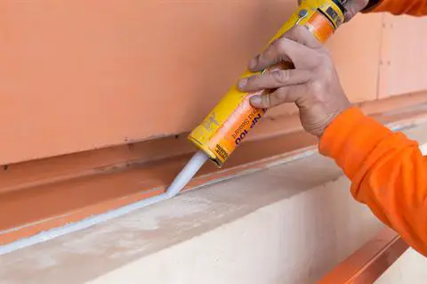A man using a caulk gun to apply building sealant at a horizontal building joint.