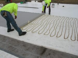 Two roofers installing a TPO single-ply roof membrane in adhesive.