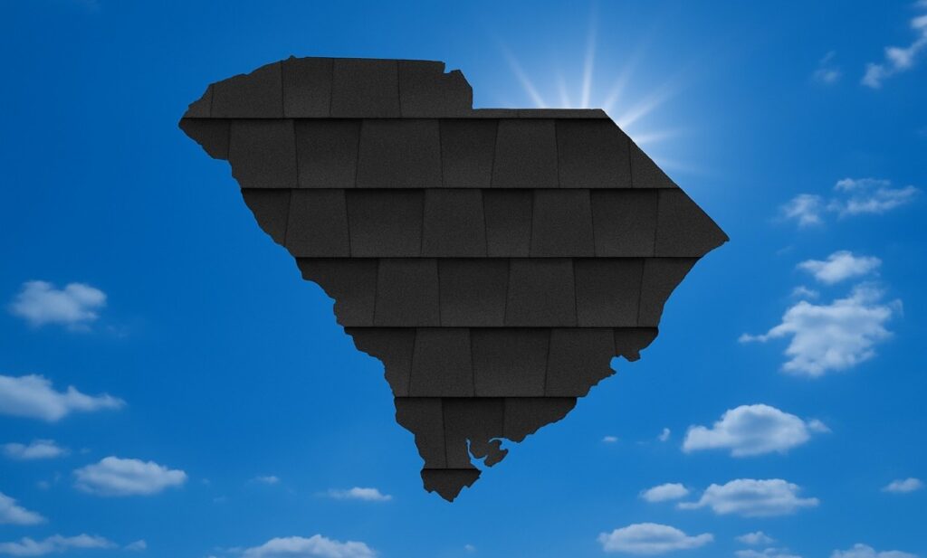 Outline of the State of South Carolina filled in with an image of asphalt shingles, set against a background of blue sky with clouds and sun.