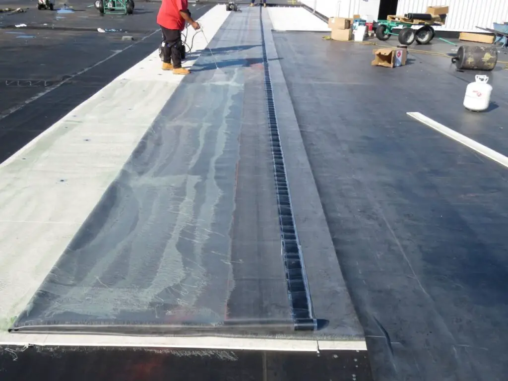 A roofer applying membrane bonding adhesive to a sheet of EPDM during the installation of a fully-adhered EPDM rubber roof.