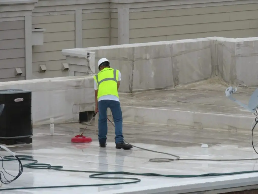 A roofer cleaning a TPO roof after 3 years of dirt build-up.