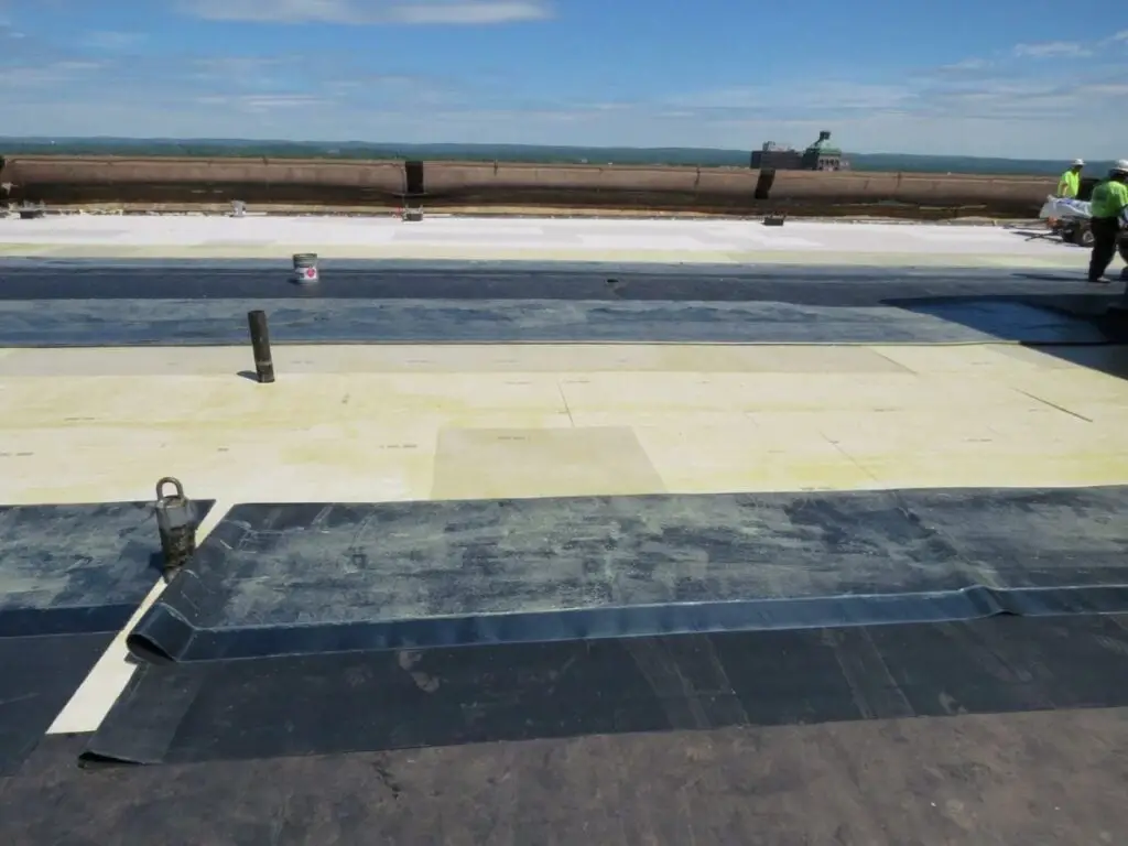 Sheets of EPDM membrane with bonding adhesive applied before the sheets of fully-adhered EPDM are rolled into position.